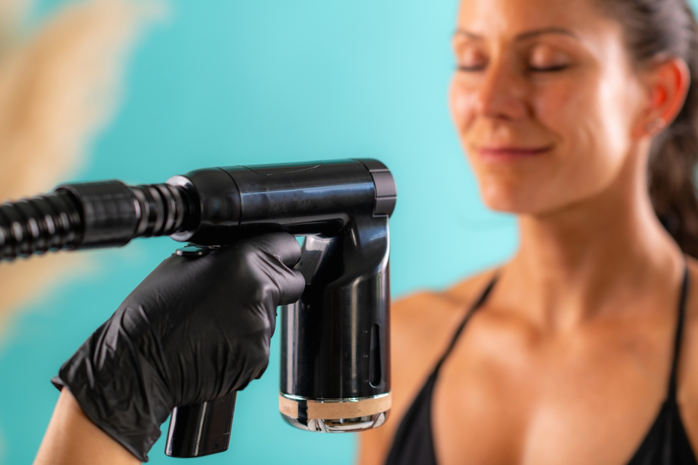 beauty,technician,applying,face,spray,tan,evenly,with,precision,tool,